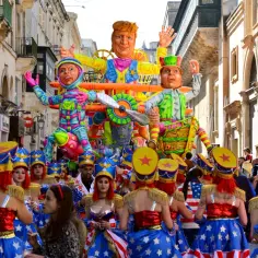 Kolorowy karnawał na Malcie w lutym. Barwne platformy i tancerki w strojach z gwiazdami i pasami maszerują ulicą.