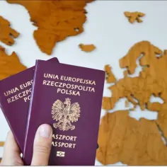 Dwa polskie paszporty, jeden z nich to paszport tymczasowy dla dziecka, na tle drewnianej mapy Europy.