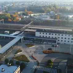Widok na nowoczesny dworzec PKP Lubliniec z parkingiem wielopoziomowym i torami kolejowymi w tle.