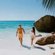 Para idealny czas na Seszele, kiedy jechać? Para spaceruje po rajskiej plaży z turkusową wodą i granitowymi skałami.
