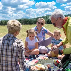 Rodzina na pikniku, ciesząca się słońcem i jedzeniem. Czas na wykorzystanie **bonów turystycznych do kiedy**!