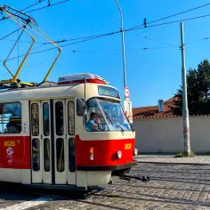Czerwono-biały tramwaj z numerem 8530 jedzie po brukowanej ulicy. Idealny sposób, by tanio do Pragi pociągiem, a potem tramwajem po mieście.