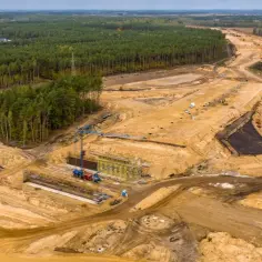 Budowa drogi w lesie, która może być częścią trasy jak dojechać do Sarbinowa. Widoczne koparki, dźwigi i plac budowy.