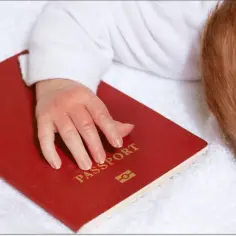 Dziecko z rudymi włosami śpi na białym ręczniku, jego dłoń spoczywa na czerwonym paszporcie. Czy do Hiszpanii potrzebny jest paszport dla malucha?