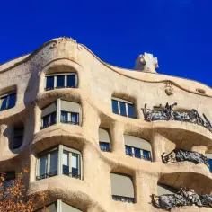 Falista fasada Casa Mila w Barcelonie, z kamienia i kutego żelaza, pod błękitnym niebem.