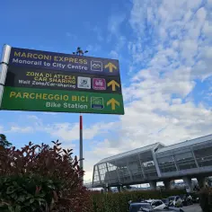 Znak drogowy informuje, jak dojechać z lotniska w Bolonii do centrum: Marconi Express (monorail), car-sharing i stacja rowerowa.