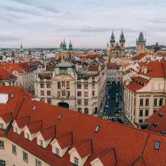 Widok na dachy Pragi, z widocznymi wieżami kościołów i ulicą z samochodami, gdzie porusza się komunikacja miejska.