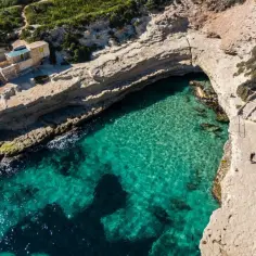 Maltańskie plaże zachwycają turkusową wodą i skalistymi zatoczkami. Dwie osoby spacerują ścieżką nad klifem, podziwiając piękno wybrzeża.
