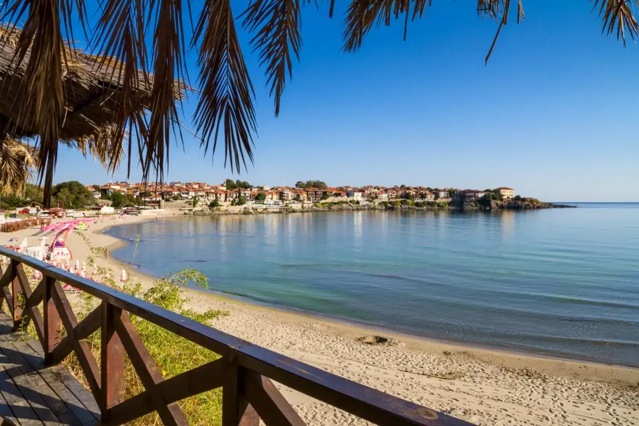 Widok na spokojne morze i piaszczystą plażę z widocznymi parasolami i budynkami w oddali. Idealne miejsce na wypoczynek na złote piaski Bułgaria.