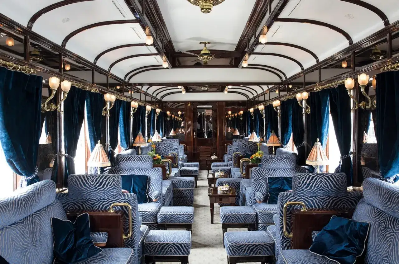 Luksusowy pociąg do Budapesztu z Polski. Wnętrze wagonu z wygodnymi fotelami w niebieskie wzory, aksamitnymi zasłonami i eleganckimi lampkami.