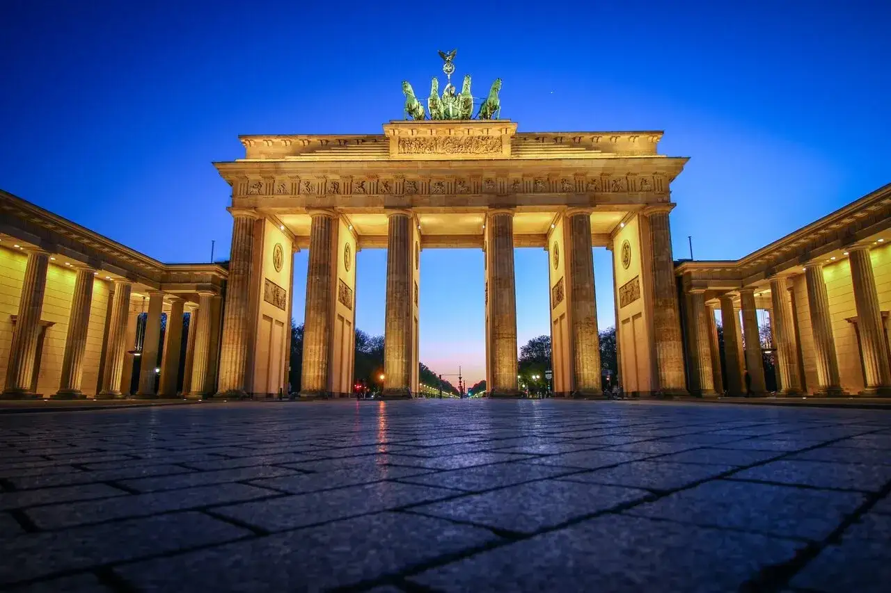 Majestatyczna Brama Brandenburska w Berlinie, oświetlona ciepłym światłem, góruje nad brukowanym placem o zmierzchu.