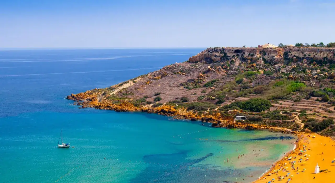 Malta oferuje piękne plaże z turkusową wodą i piaszczystym brzegiem. Widok na zatokę z łodzią i turystami.