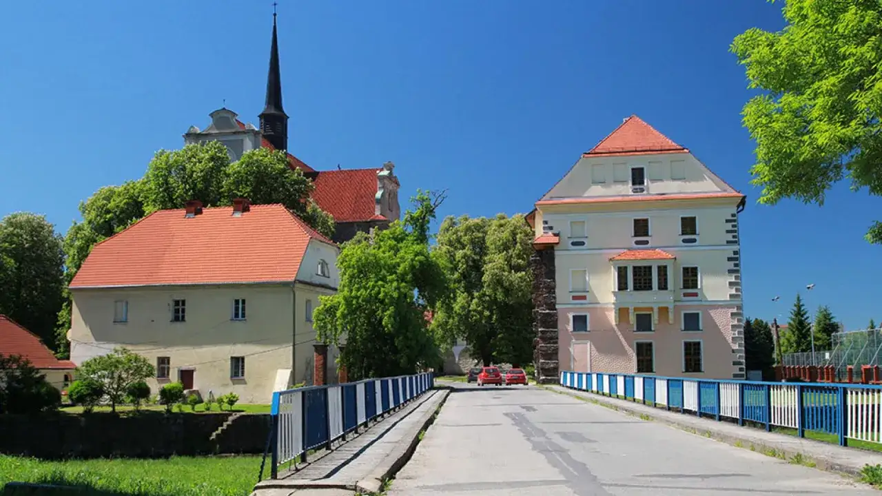 Most na rzece, zamek i kościół – to główne kamieniec ząbkowicki atrakcje. W tle wieża kościelna i zielone drzewa.
