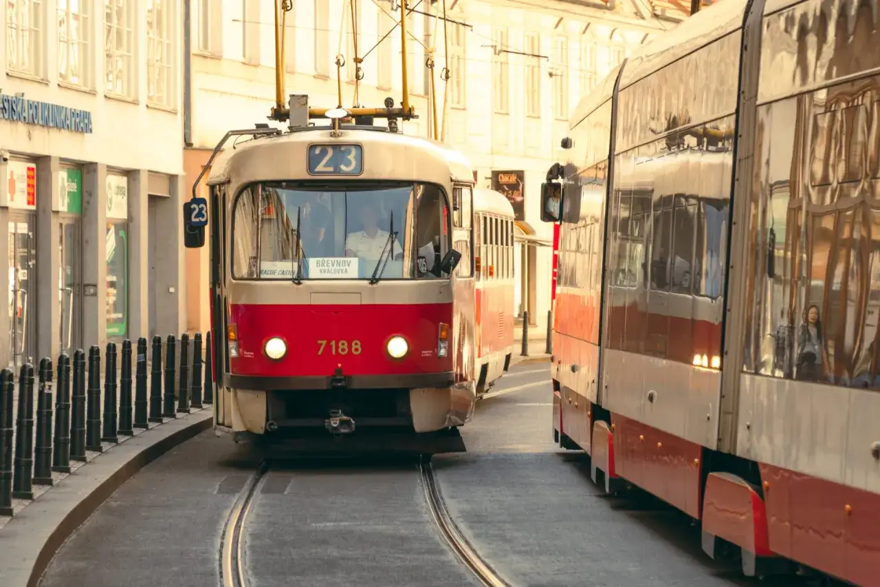 Dwa tramwaje jadące po torach w Pradze. Jeden z nich, czerwono-kremowy, ma numer 23 i tabliczkę