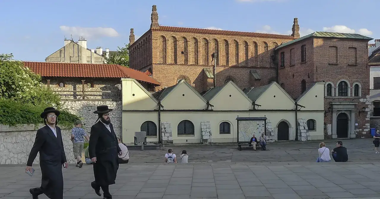 Kazimierz Kraków atrakcje: dwaj mężczyźni w tradycyjnych strojach żydowskich spacerują po placu przed zabytkowymi synagogami.