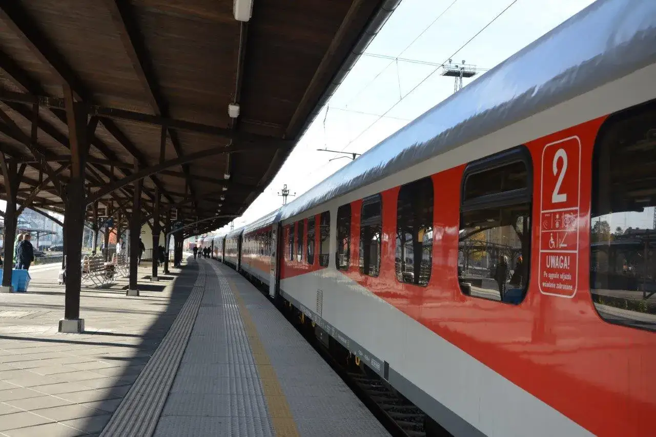 Dworzec PKP Jaworzyna Śląska. Czerwono-biały pociąg stoi na peronie pod drewnianą wiatą.