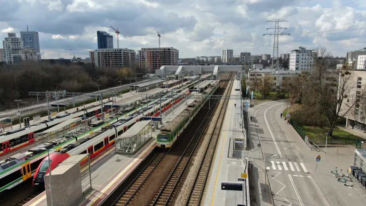Wielopoziomowy dworzec Warszawa Gdańska z wieloma pociągami na torach i nowoczesnymi budynkami w tle.