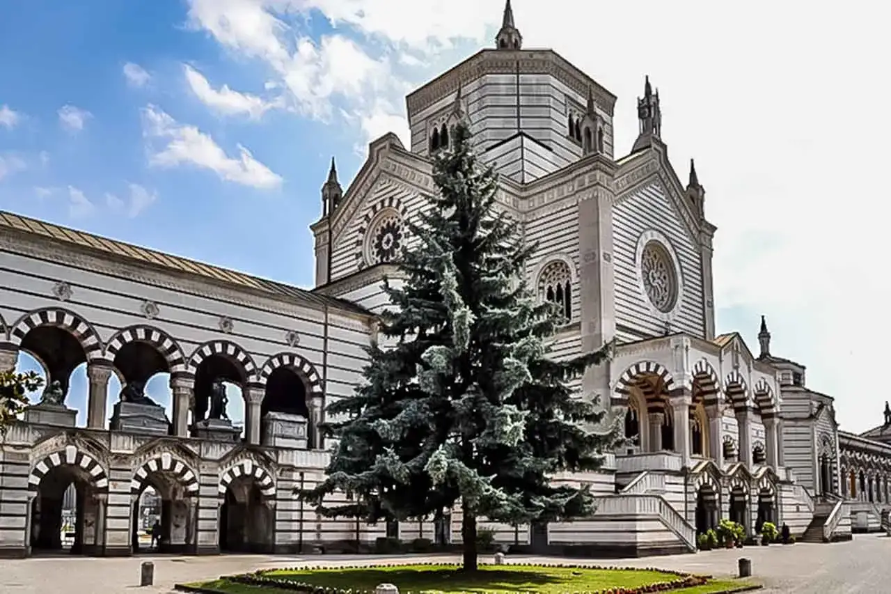 Monumentalny cmentarz w Mediolanie, z imponującą architekturą i wiecznie zielonym drzewem na pierwszym planie.