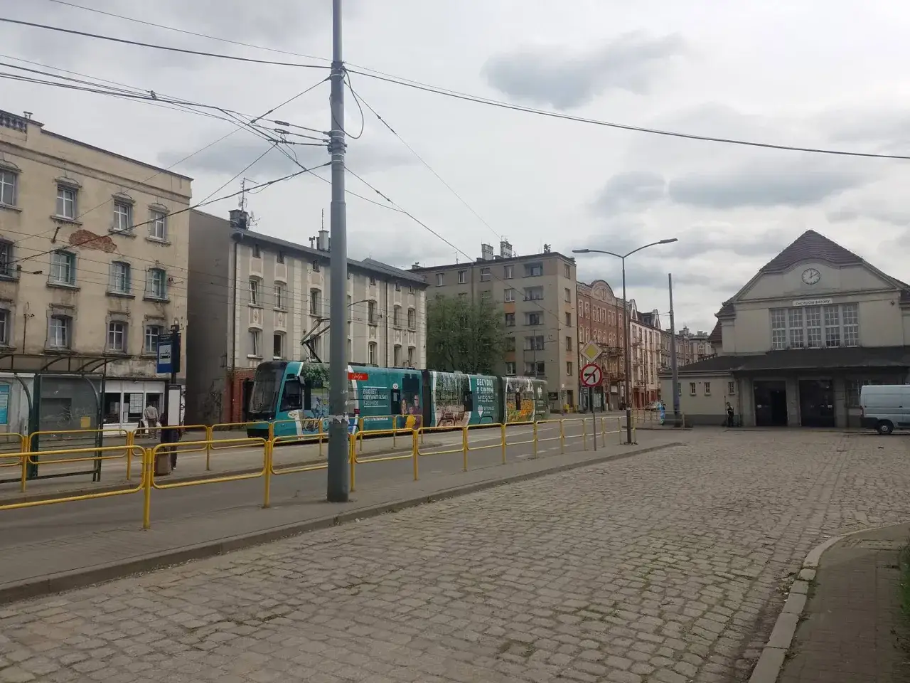 Chorzów miasto dworzec PKP. Tramwaj z reklamami na tle kamienic i dworca kolejowego.