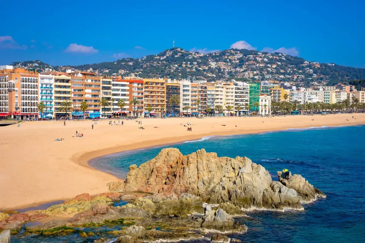 Słoneczna plaża w Lloret de Mar z kolorowymi budynkami i górami w tle. Wspaniałe lloret de mar atrakcje czekają!
